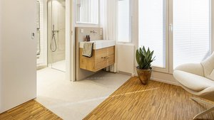 Ein modernes Badezimmer mit einem Holzwaschtisch, einer Dusche und großen Fenstern, die viel Tageslicht hereinlassen.
