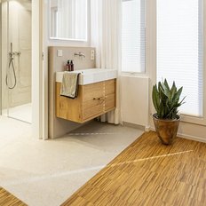 Ein modernes Badezimmer mit einem Holzwaschtisch, einer Dusche und großen Fenstern, die viel Tageslicht hereinlassen.