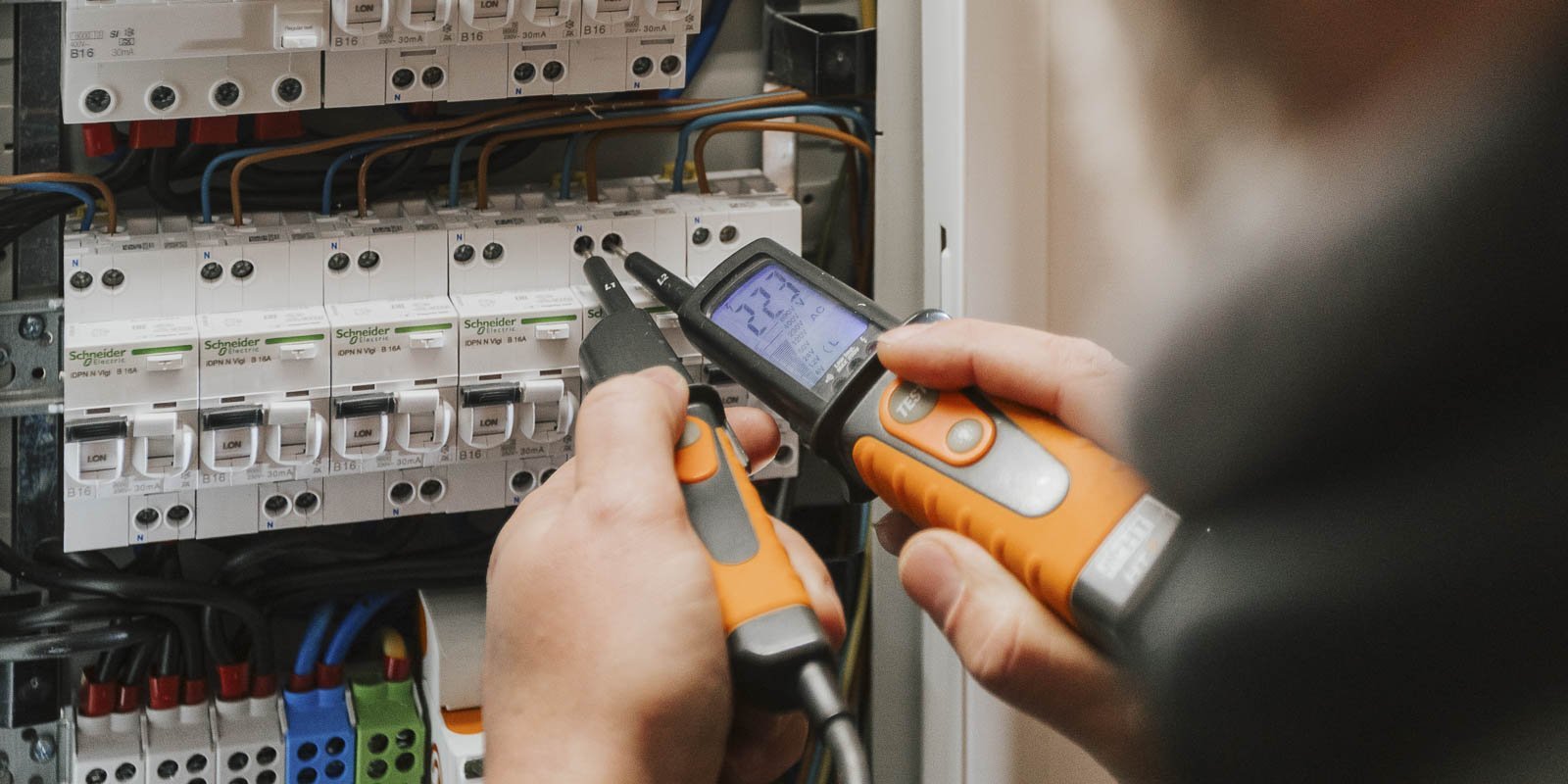 Eine Person überprüft elektrische Schaltkreise mit einem Multimeter und einem Prüfgerät in einem Sicherungskasten.