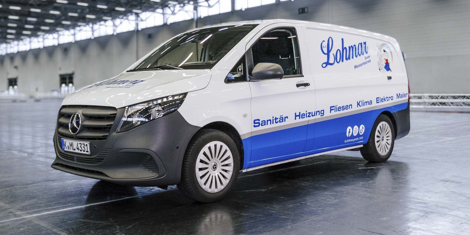 Ein moderner Lieferwagen mit dem Logo von Lohmar, der in einem großen, hellen Raum geparkt ist.