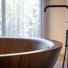 Eine elegante, runde Badewanne aus Holz steht im hellen Raum mit großen Fenstern, die sanftes Licht hereinlassen.