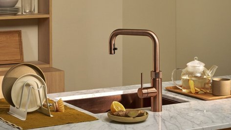 Eine moderne Küche mit einem kupferfarbenen Wasserhahn und einem eleganten Marmortisch, auf dem eine Teekanne steht.
