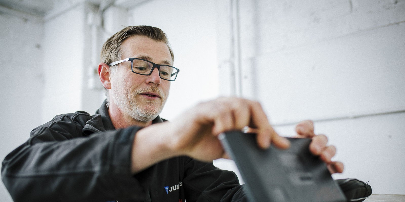 Ein Mann mit Brille und Bart konzentriert sich auf ein Tablet, während er in einem hellen Raum arbeitet.