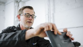 Ein Mann mit Brille und Bart konzentriert sich auf ein Tablet, während er in einem hellen Raum arbeitet.