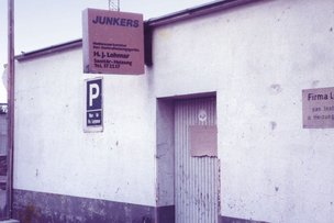An der Wand des Gebäudes sind zwei Schilder angebracht, eines für die Firma Lohmar und das andere für Junkers Heizgeräte.