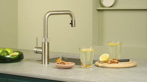 Eine moderne Küchenzeile mit einem eleganten Wasserhahn, frischen Zitrusfrüchten und einem Glas mit Zitronenwasser auf der Arbeitsplatte.
