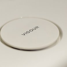 Ein runder, weißer Knopf mit der Aufschrift 'VIGOUR' auf einer hellen Oberfläche, die minimalistisch wirkt.