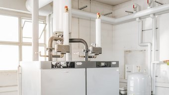 Zwei große Heizkessel stehen in einem hellen Raum, umgeben von Rohren und einem großen Druckbehälter.