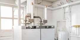 Zwei große Heizkessel stehen in einem hellen Raum, umgeben von Rohren und einem großen Druckbehälter.
