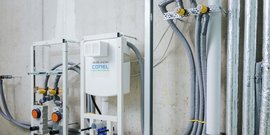 An einer Wand montierte Rohre und Anschlüsse, die für die Installation von Sanitär- oder Heizungsanlagen vorbereitet sind.