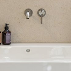 Zwei Flaschen mit Handseife und Handbalsam stehen auf einem modernen Waschbecken, umgeben von einer schlichten Wand.