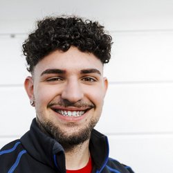 Der Mann zeigt ein breites Lächeln, seine Augen strahlen vor Freude, während er in einem sportlichen Outfit posiert.
