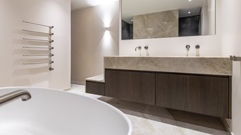 Ein modernes Badezimmer mit einer eleganten Holzwaschtischplatte und zwei Wasserhähnen, die an einer hellen Wand montiert sind.