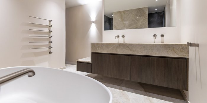 Ein modernes Badezimmer mit einer eleganten Holzwaschtischplatte und zwei Wasserhähnen, die an einer hellen Wand montiert sind.