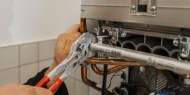 Ein Handwerker arbeitet mit einer Zange an einer Heizungsanlage, um eine Rohrverbindung zu sichern.