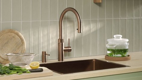 Eine moderne Küche mit einem eleganten Kupferwasserhahn, frischem Gemüse und einem Glasbehälter auf der Arbeitsplatte.
