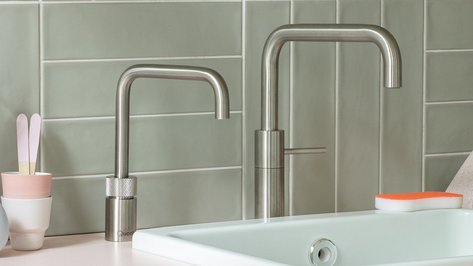 Eine moderne Küchenszene mit zwei stilvollen Wasserhähnen und einem hellen Spülbecken, umgeben von dekorativen Objekten.