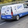 Lohmar Sanitärfahrzeug in Bewegung auf der Hauptstraße Ein Lieferwagen mit dem Logo von Lohmar fährt schnell auf einer Straße, umgeben von Bäumen und einem Zaun im Hintergrund.
