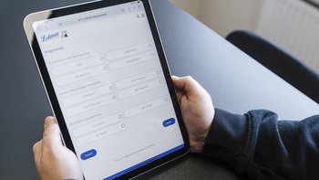 Das Bild zeigt eine Hand, die ein Tablet mit einem Online-Formular für Heizungsinformationen bedient, auf einem Tisch.