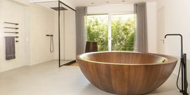 Ein modernes Badezimmer mit einer großen, runden Holzbadewanne und einem Blick auf einen grünen Garten durch große Fenster.